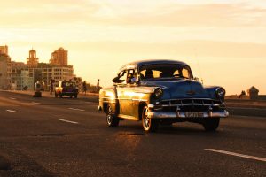 Ein Auto im Retrolook fährt, während eines Sonnenuntergangs, eine Straße entlang.